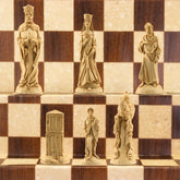 The Ivory/Cream side of a handcrafted chess set featuring characters from the Arthurian legend, placed on a checkered board. The set includes figures representing King Arthur, Queen Guinevere, Merlin the Magician, Sir Lancelot the Knight, & the Castle of Camelot as the rook.