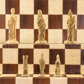 The ivory coloured side of a handmade chess set depicting Roman era figures, displayed on a wooden chess board.