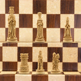 The ivory coloured side of a handmade miniature chess set with pieces crafted in the design of a typical Western European court in the Middle Ages. The costumes and architecture of the period are faithfully reproduced.
