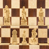 A close-up of a handmade chess set with pieces designed in Celtic and Viking styles, set up on a wooden chess board.