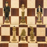 The cream base, gold accented side of a nautical-themed hand painted chess set with pieces including a Captain, Mermaid, Navigator, Seahorse, Lighthouse, and Ship, displayed on a brown and beige chess board.