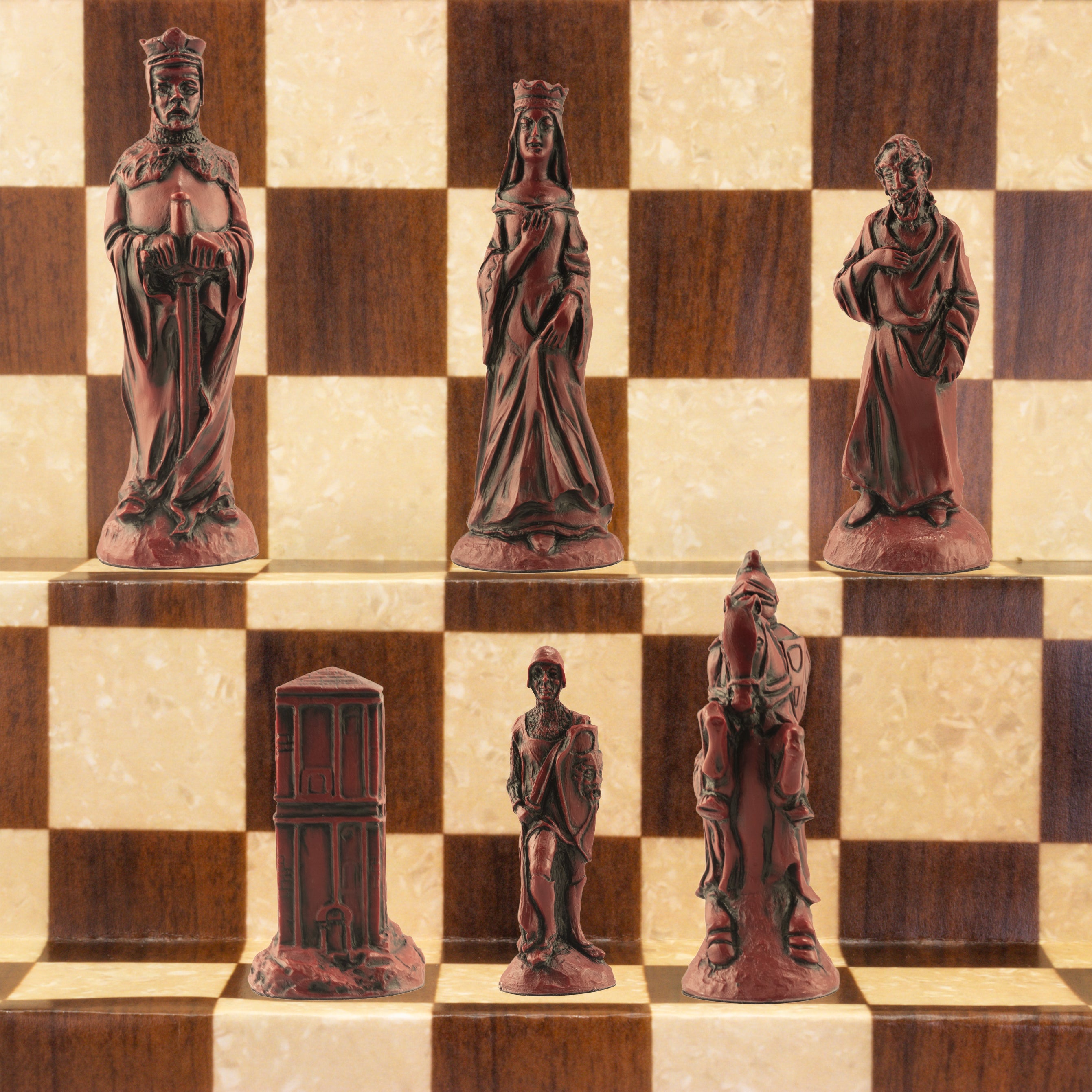 The Burgundy/Red side of a handcrafted chess set featuring characters from the Arthurian legend, placed on a checkered board. The set includes figures representing King Arthur, Queen Guinevere, Merlin the Magician, Sir Lancelot the Knight, & the Castle of Camelot as the rook.