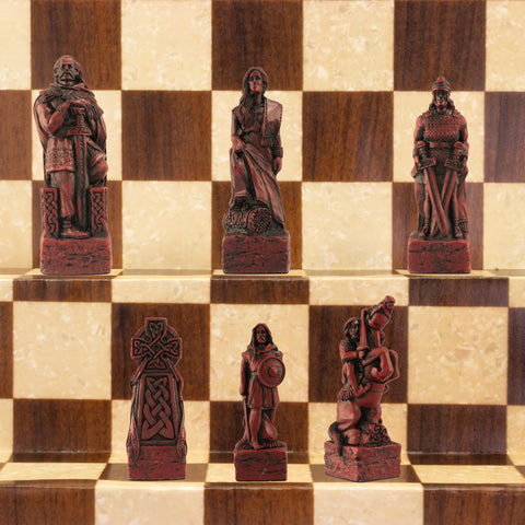 A close-up of a handmade chess set with pieces designed in Celtic styles, set up on a wooden chess board.