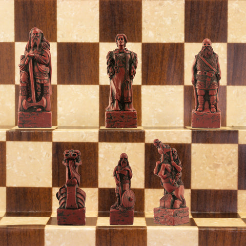 A close-up of a handmade chess set with pieces designed in Viking styles, set up on a wooden chess board.