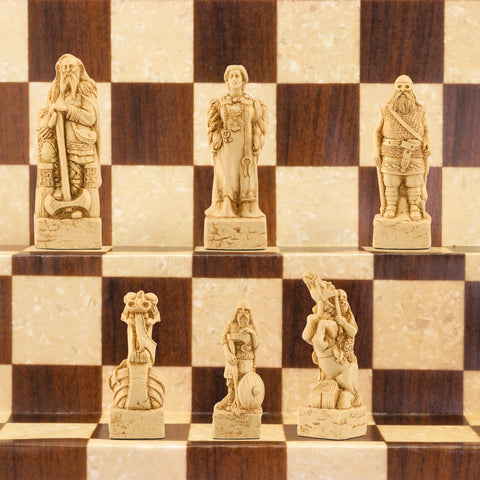 A close-up of a handmade chess set with pieces designed in Viking styles, set up on a wooden chess board.