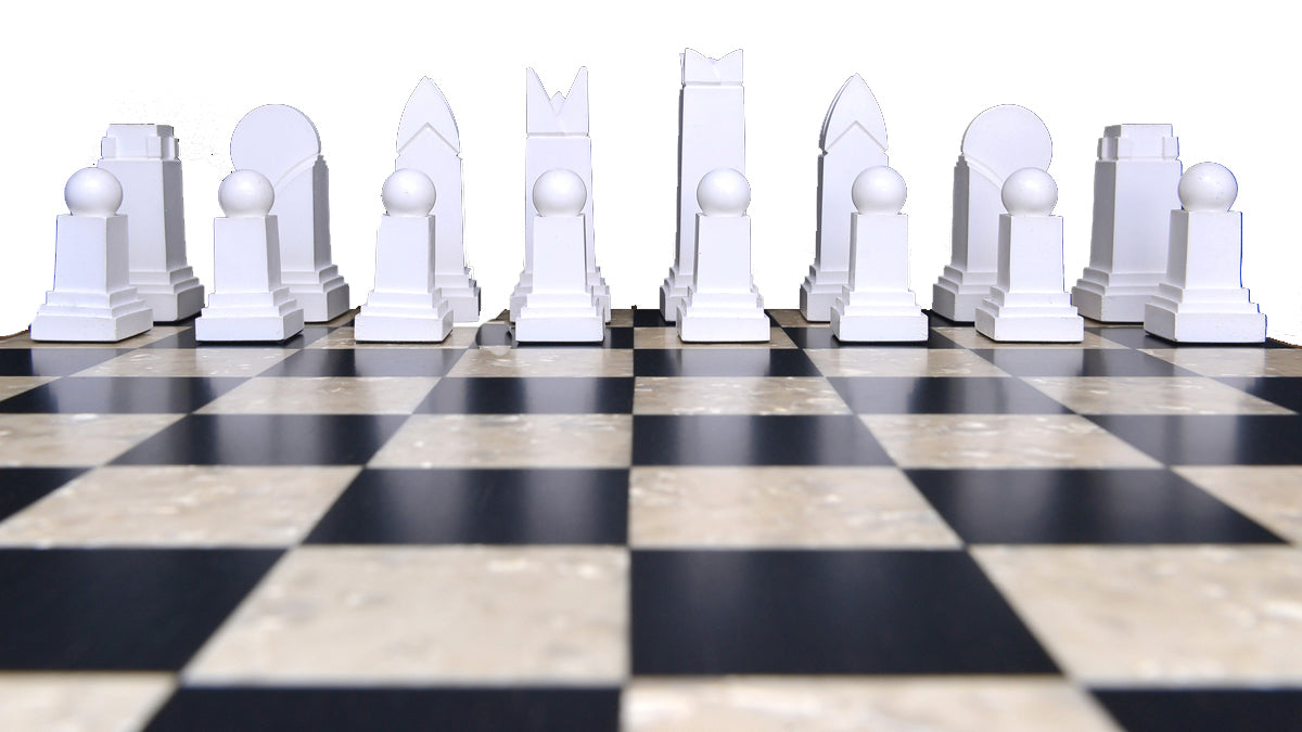The white side of a handmade chess set displayed on a checkered board. The set includes various shapes of pieces, such as rooks, knights, bishops, and pawns, showcasing an Art Deco design style.