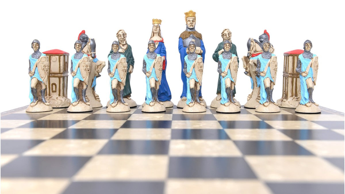 A shot showing the full Blue side of a handpainted chess set featuring characters from the Arthurian legend, placed on a checkered board. The set includes figures representing King Arthur, Queen Guinevere, Merlin the Magician, Sir Lancelot the Knight, & the Castle of Camelot as the rook.