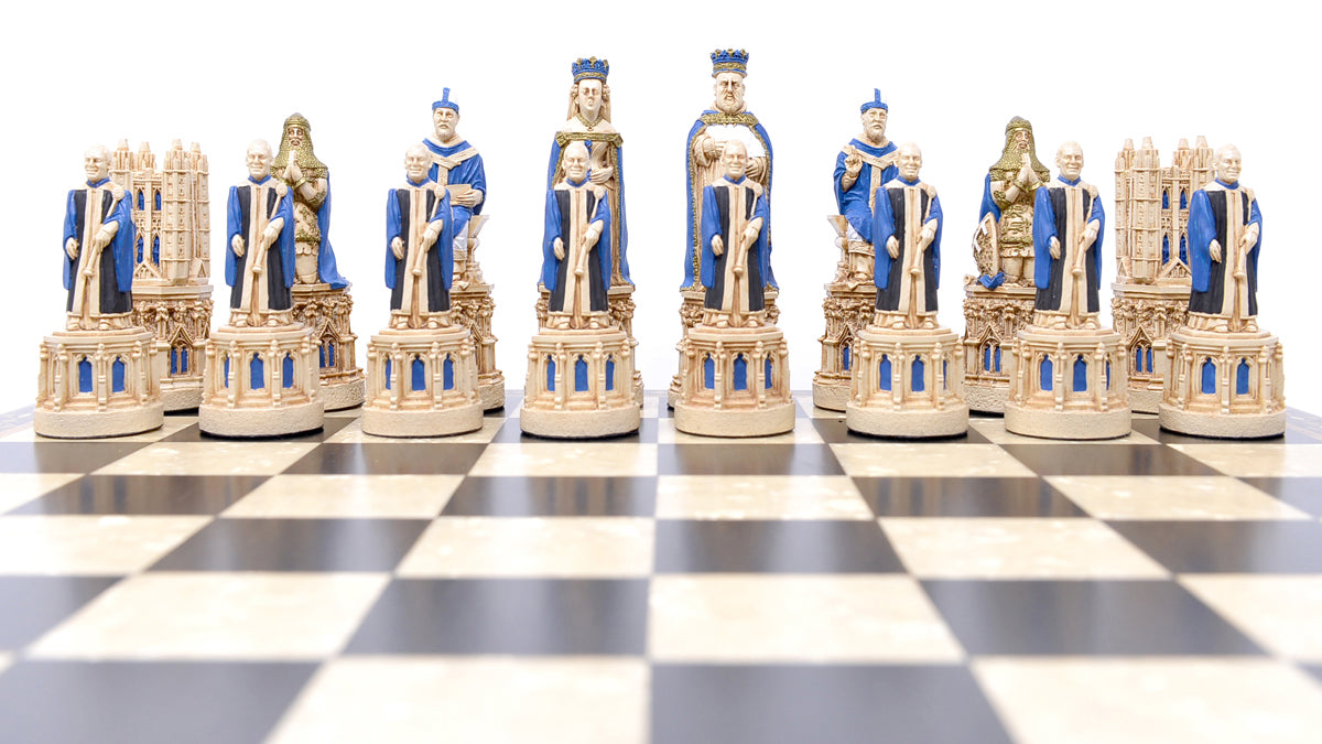 The blue coloured side of a hand painted chess set inspired by the architecture and statuary in and around Medieval Cathedrals, a chess set of gracious proportions and great detail, Displayed on a black and white chess board.